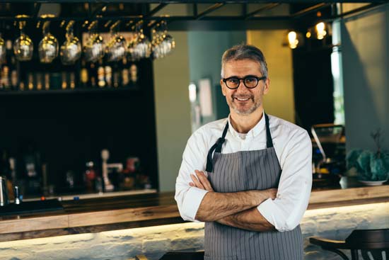 Bar manager, stood in front of his wooden bar with glasses and wine displayed behind