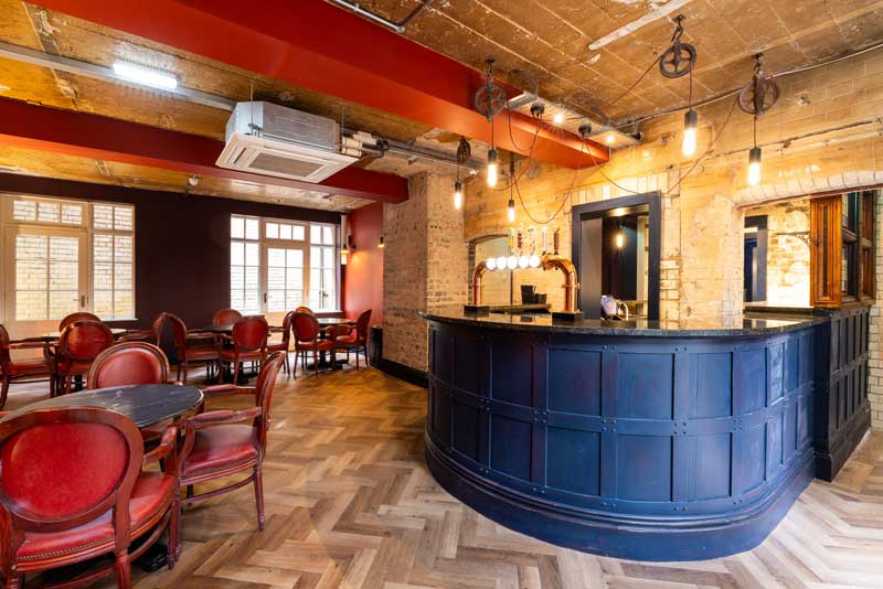 White-lion-stockport-bar-commercial-refit Exposed brick work features in the room with red painted exposed iron lintels. A rich blue bar are is complimented by dark red antique furnishings